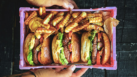 A person holding a container with 3 plant-based burgers and fries