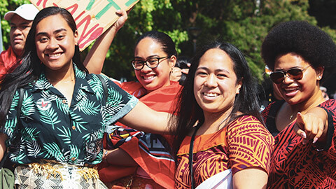 A group of young Pasifika women smiling and laughing together, outside on asunny afternoon