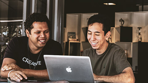 Two colleagues sitting together at a desk, working on a project on one of their laptops