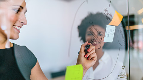 2 colleagues brainstorming with sticky notes on a glass wall