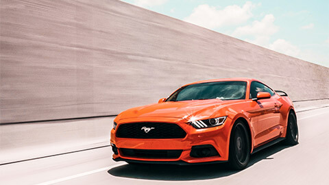 A cherry red Mustang cruising down a highway on a sunny afternoon