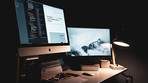 A 2 monitor setup on a desk in a dark room