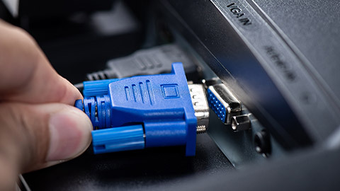 A close view of a VGA cable being put into the back of a computer