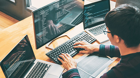 Over-the-shoulder view of a programmer working on multiple computers