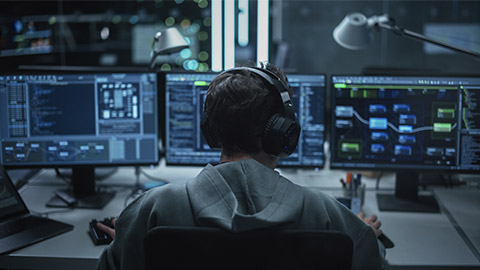 System Administrator Working in a Dark Research Facility on a Computer with Multiple Displays.