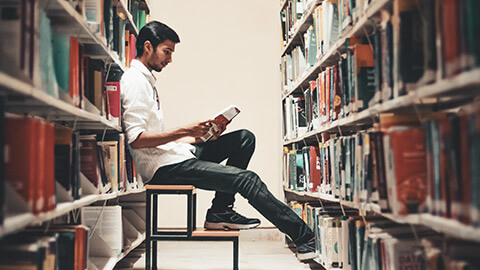 A designer sitting in a library reading a book