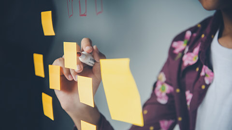 A person writing on a sticky note on a glass wall