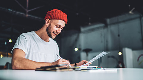 A smiling hipster working on a project at a table in an office