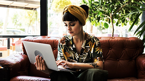 A person reading on the laptop in a leather couch.