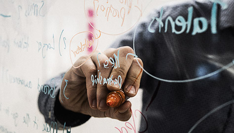 A close up shot of a person writing on a glass/white board