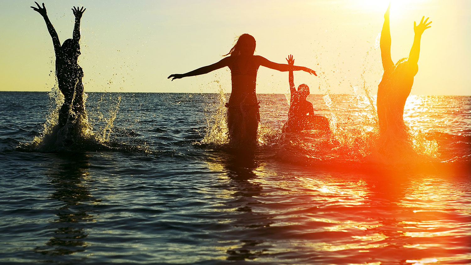 Silhouettes of young group of people jumping in ocean at sunset