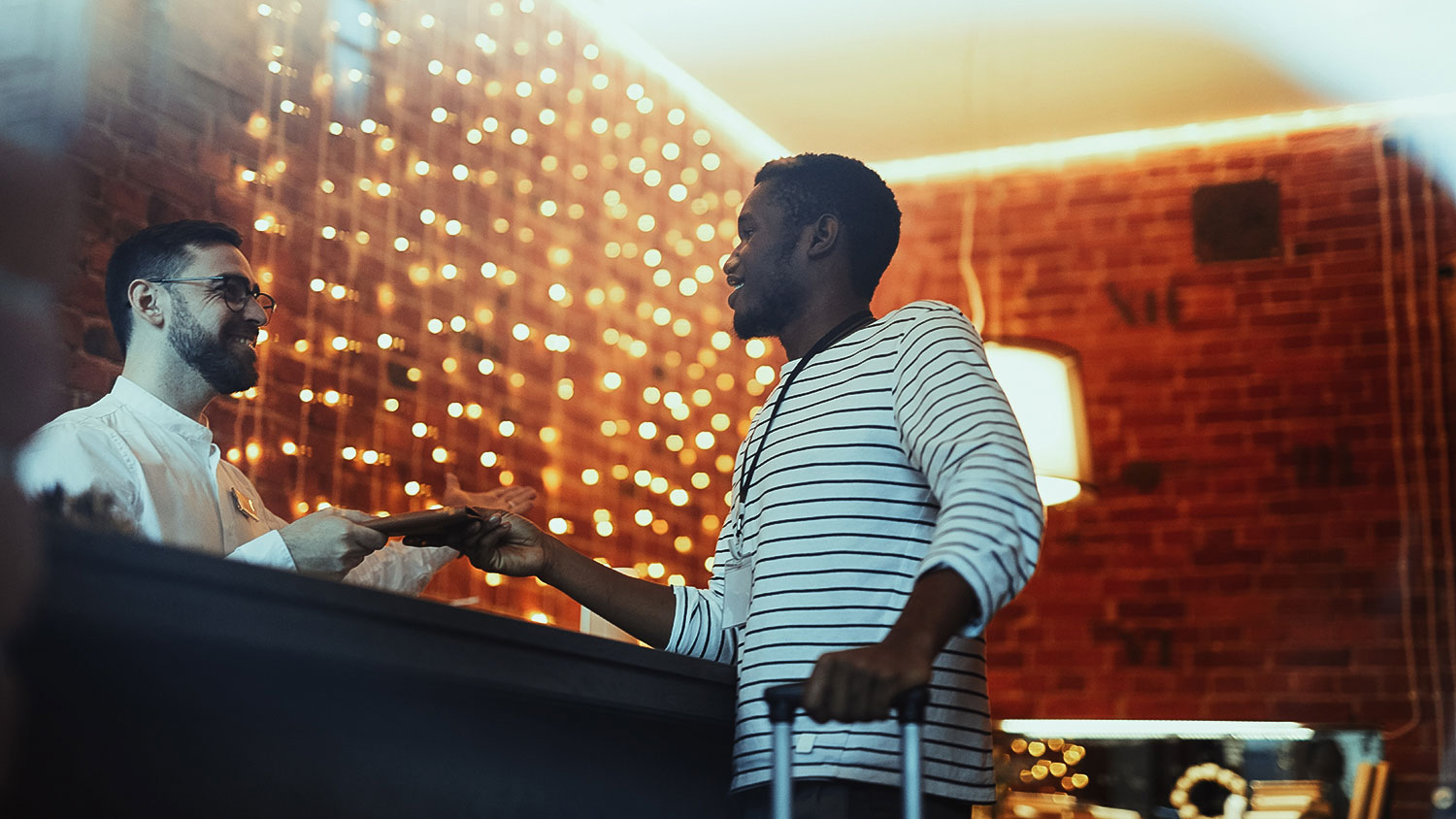 Young African-american traveler consulting with hotel receptionist by counter during accommodation