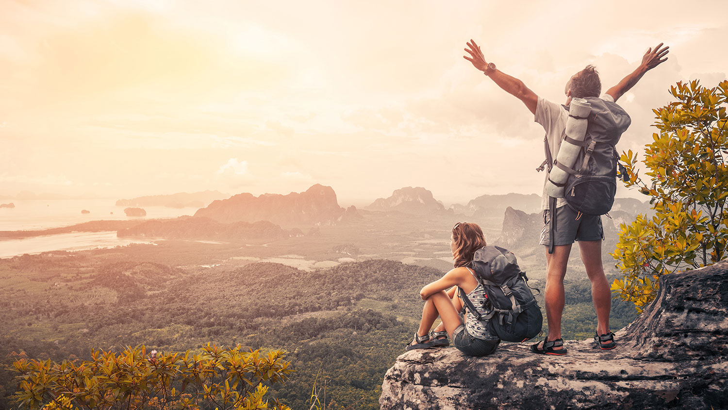 Hikers with backpacks relaxing on top of a mountain and enjoying the view of valley at sunset