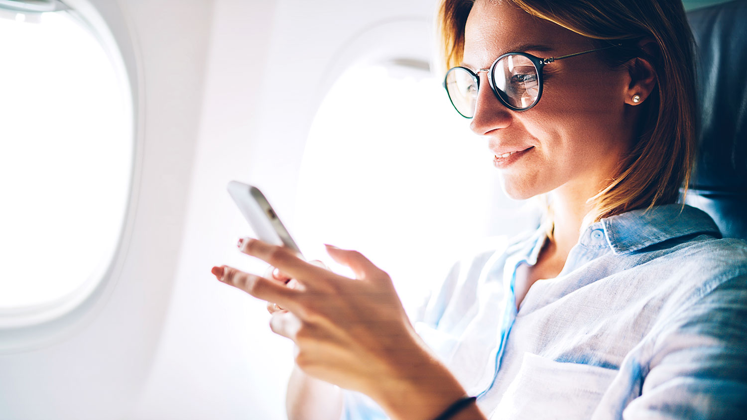 Attractive female passenger of airplane read news from networks via smartphone and wifi on board, young woman sending message on phone traveling by plane in first class connecting to wireless on phone