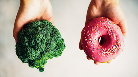 Person holding a donut and bunch of brocolli