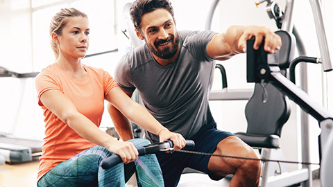 Male personal trainer with female client on rowing machine