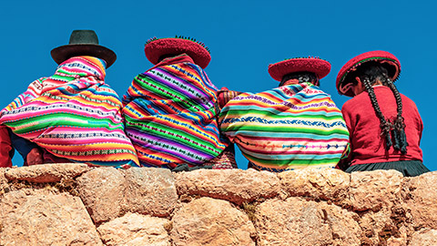 peruvian ladies wearing traditional outfits sitting on a wall