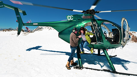 tourist being assisted out of a helicopter on a glacier