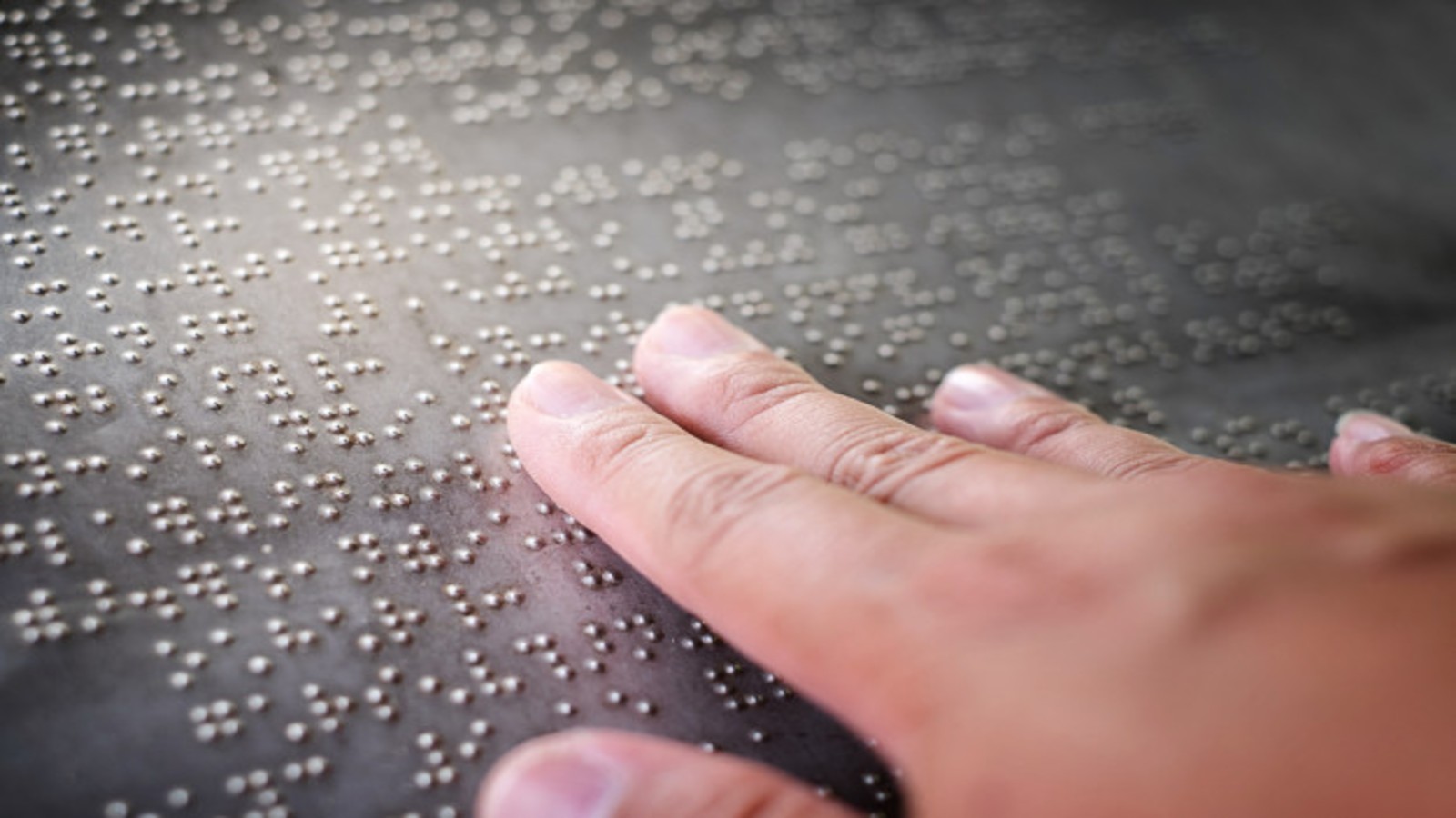 Fingers touching braille letters on a metal information sign.