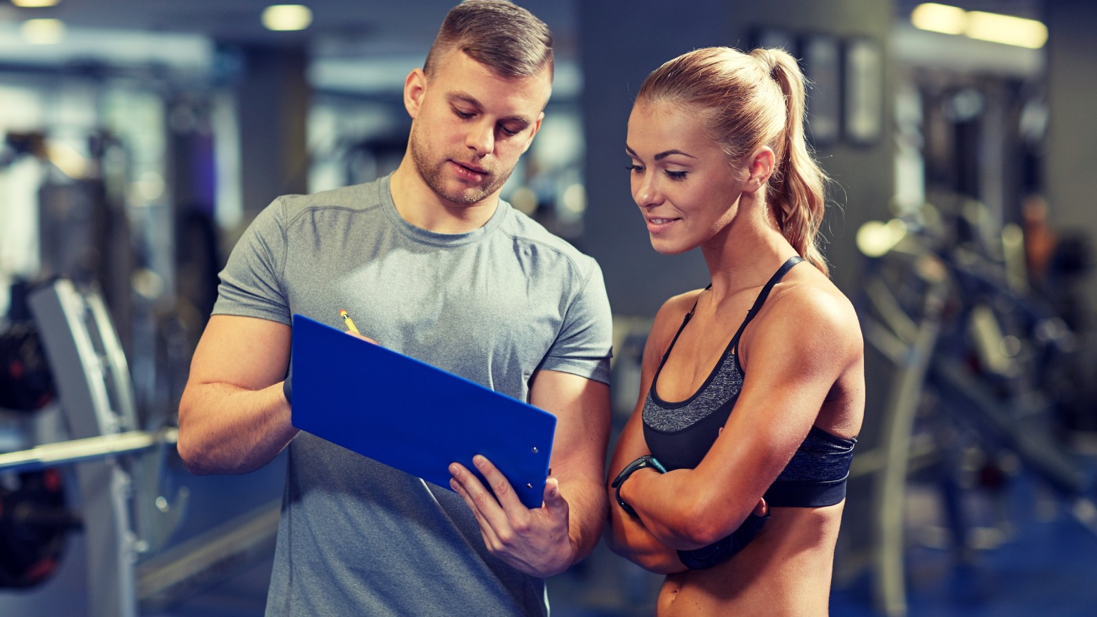 Male fitness professional reviewing progress information on a clipboard with a female client 