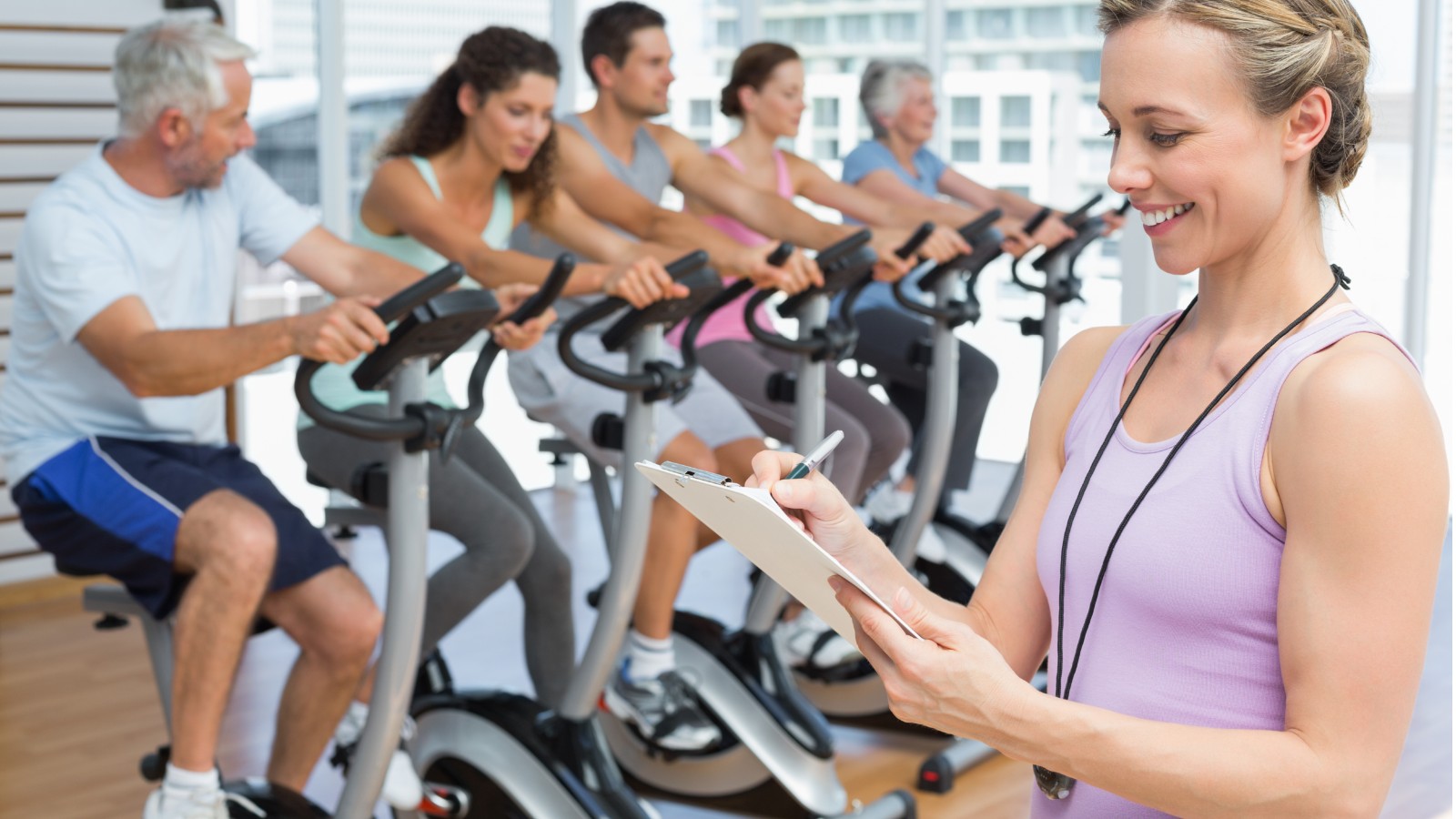 Female trainer monitoring clients on exercise bikes