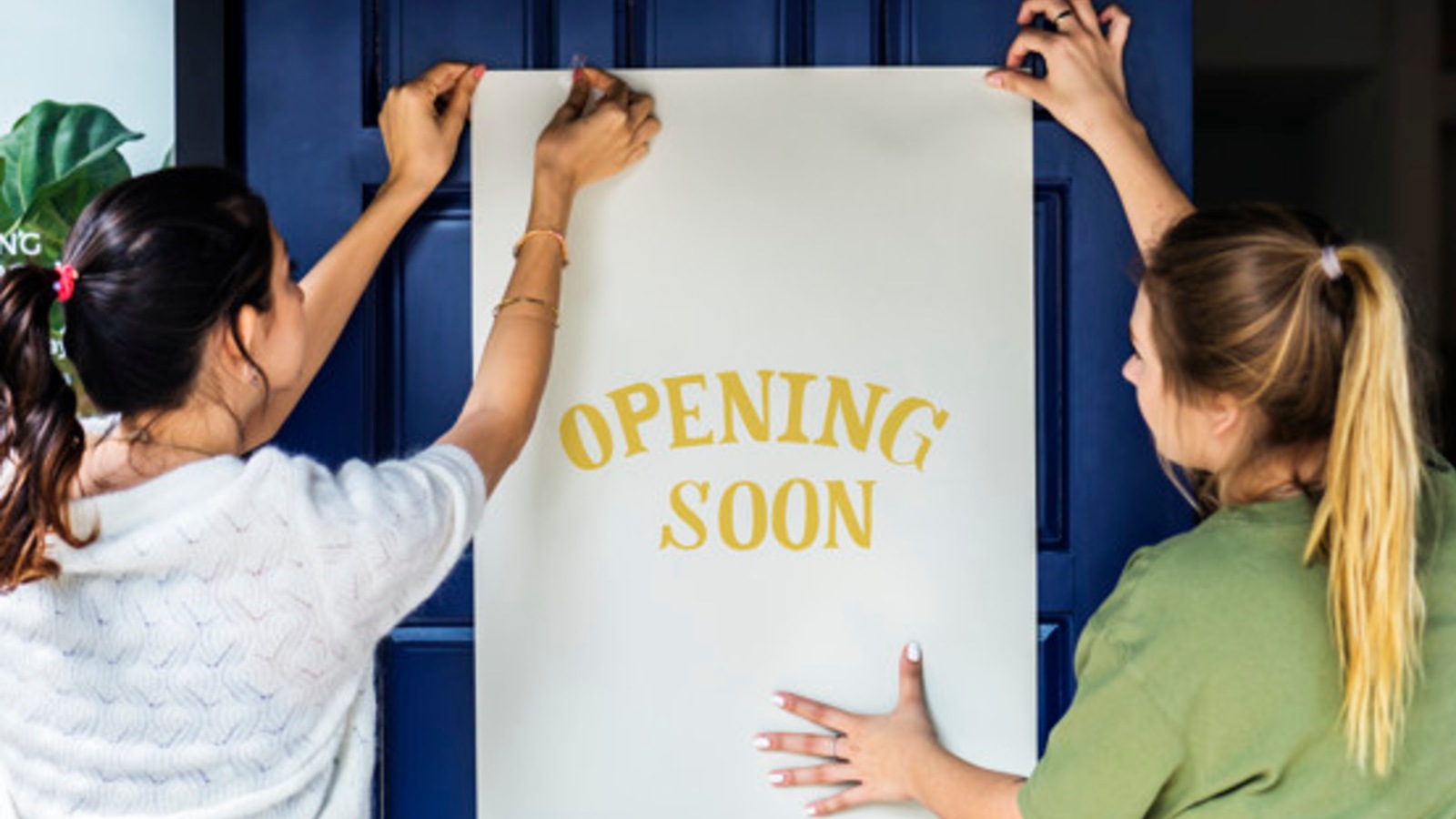 two women pinning up an opening soon sign