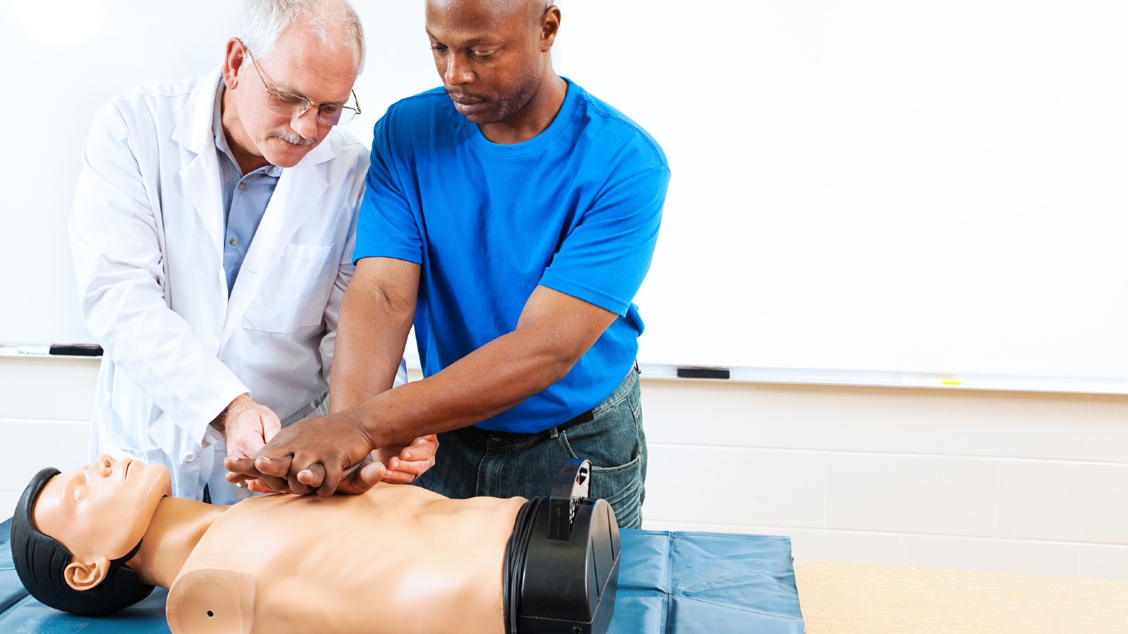 Doctor instructing a man on how to perform CPR on a manikin during a first aid class