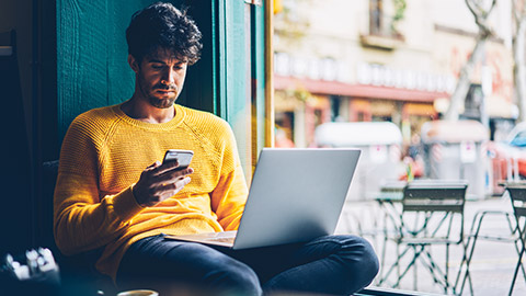 Young male sitting in a cafe accessing mobile and laptop devices