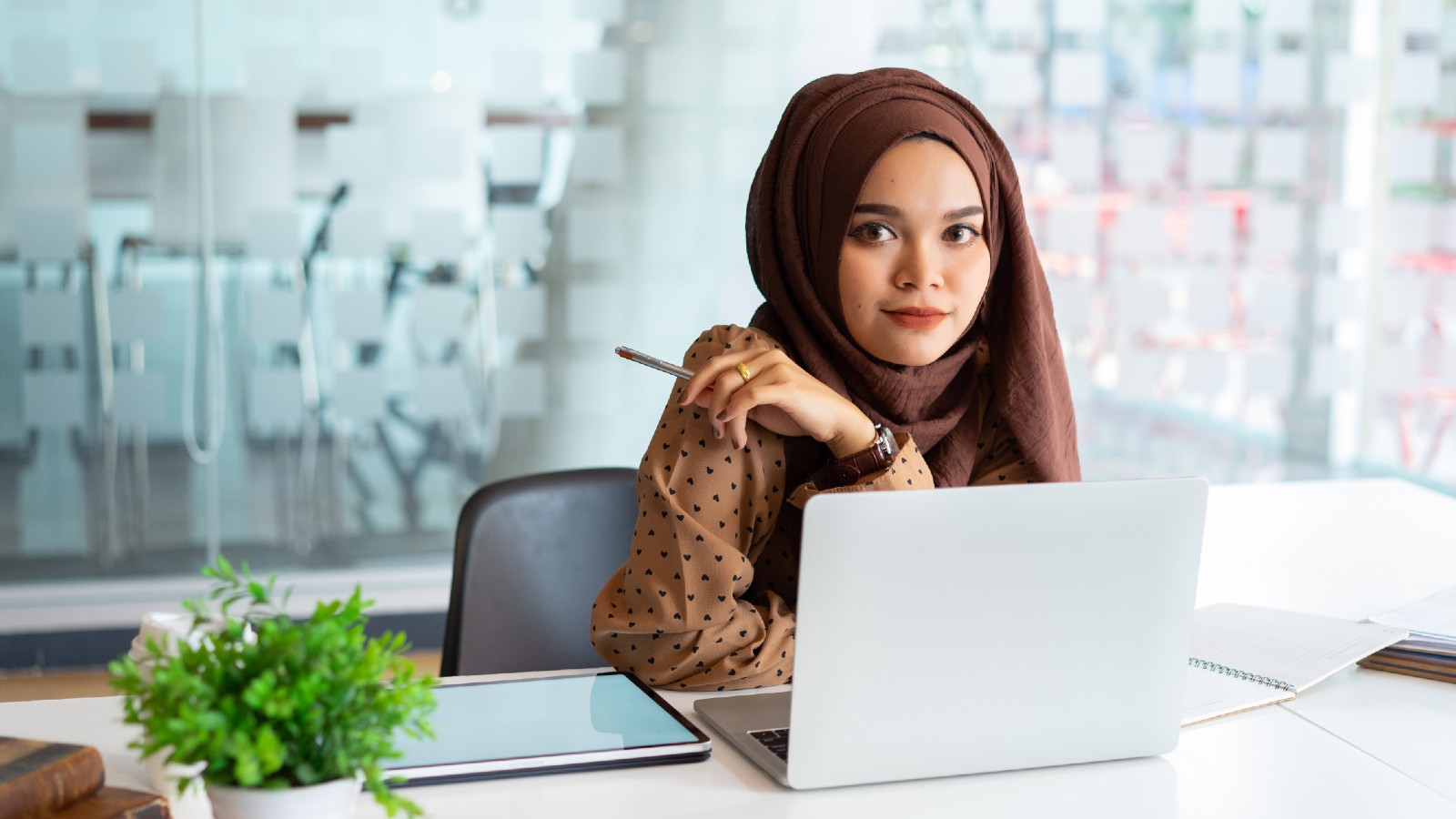 Young woman, wearing an Islamic headdress, sitting at a desk infront of a computer.