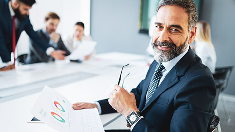 Senior male business executive sitting at a desk with a sheet of paper in his hand