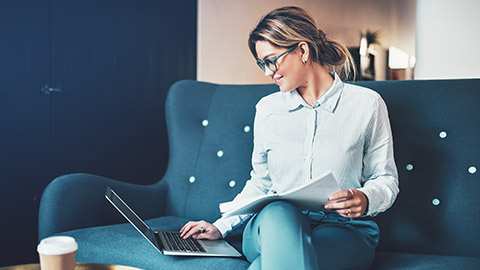 A Young accountant sitting on a couch checking a finacial report on their laptop