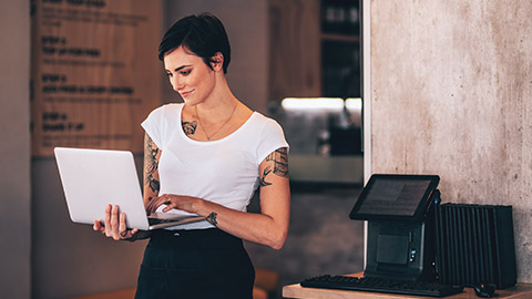 A cafe owner standing and holding a laptop while inputting information