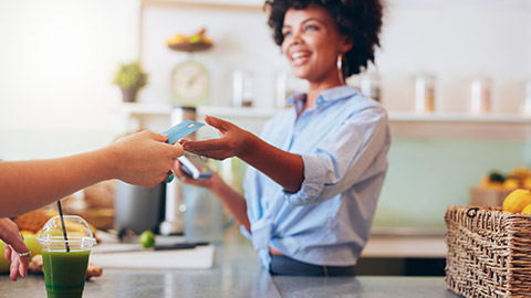 A customer in a smoothie shop handing over her card to be scanned for payment