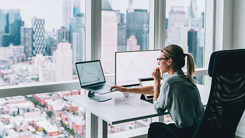 A young accountant working on a laptop in a modern office, overlooking a city skyline