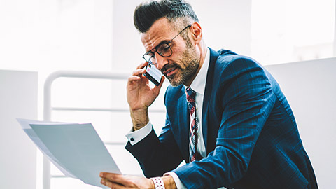 An accountant looking over documents while talking on his mobile phone