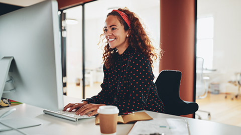 A young smiling accountant working on a large desktop computer in a modern office