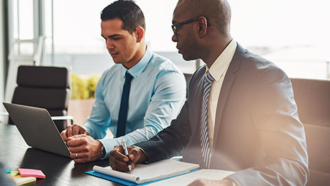 2 male work colleagues sitting at a desk checking over a financial report