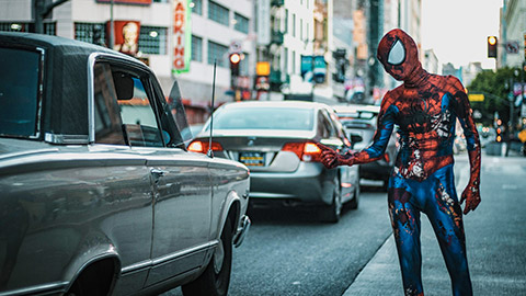 Spiderman guy thumbing a ride on city street