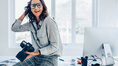 Young female sitting on desk whie holding camera