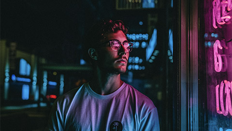 A man reading a neon sign in a store front, at night